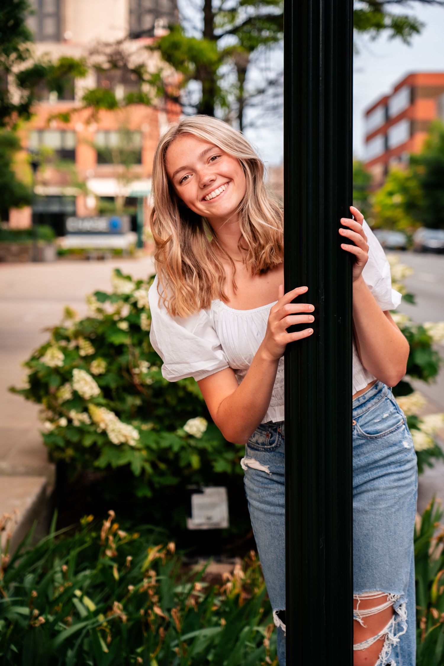 Person in casual denim outfit posing playfully between black posts outdoors.