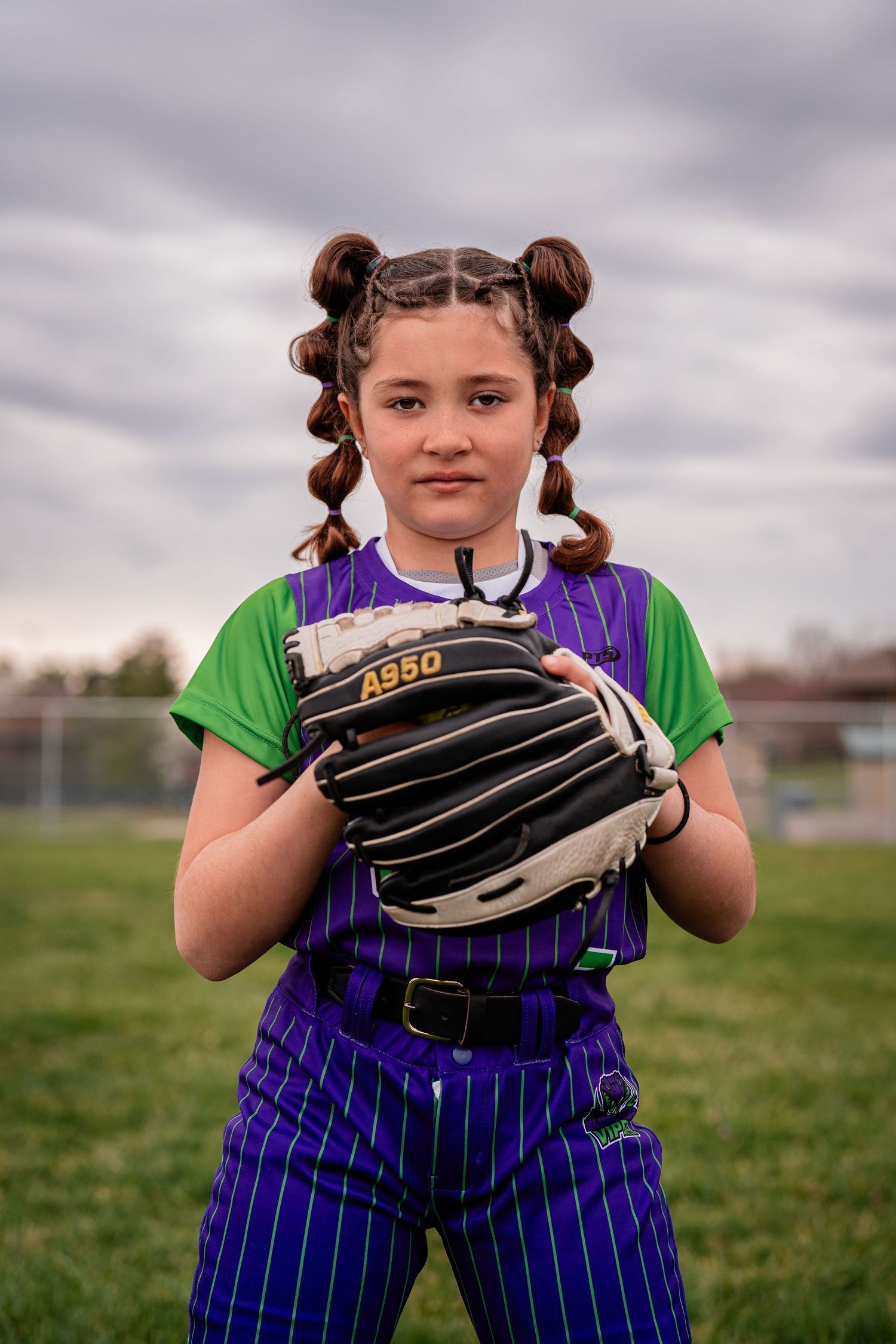 Youth softball player in purple striped uniform holds up glove on baseball field.