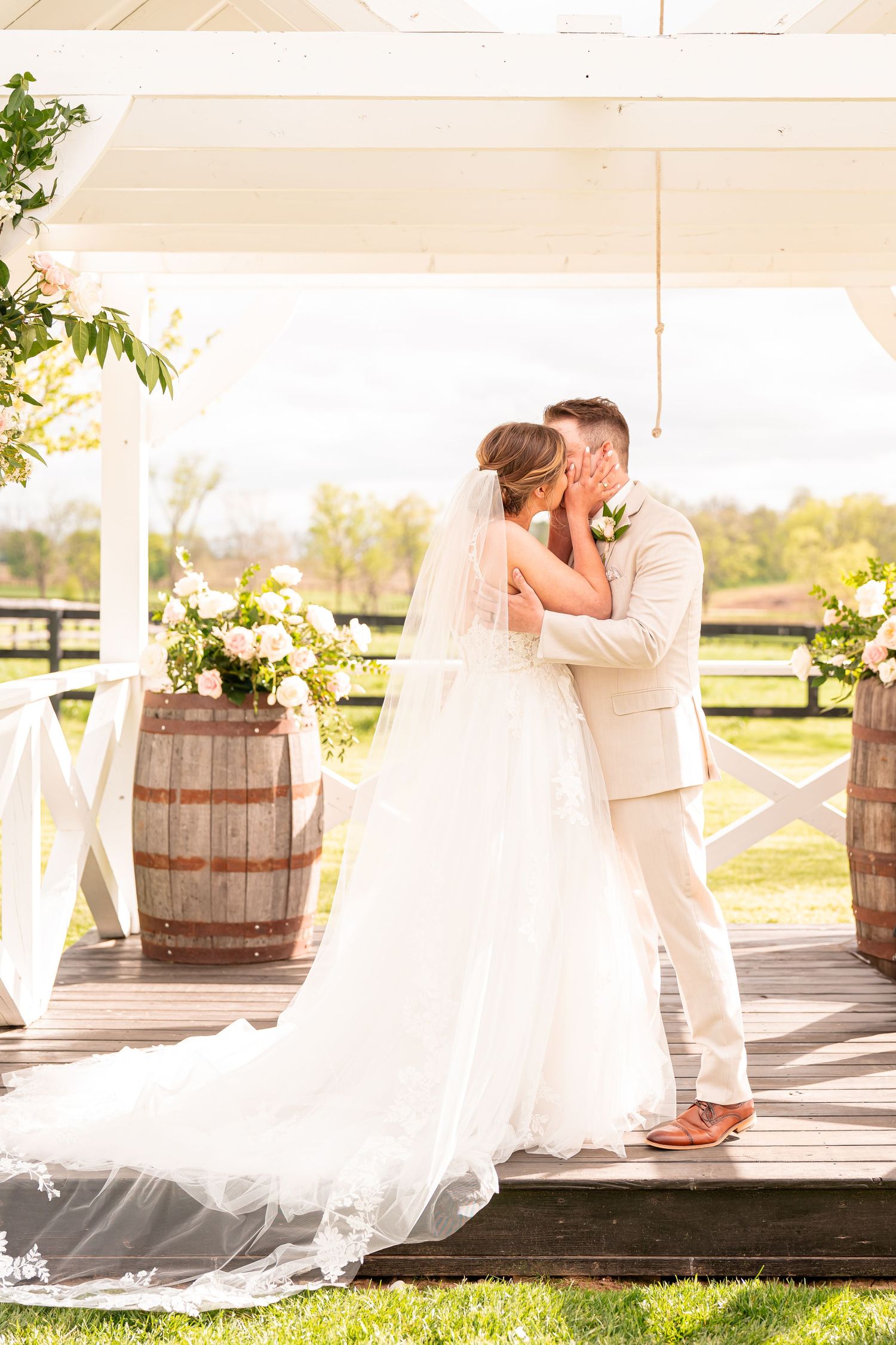 Wedding couple sharing intimate moment on rustic wooden deck with barrels and floral decor.