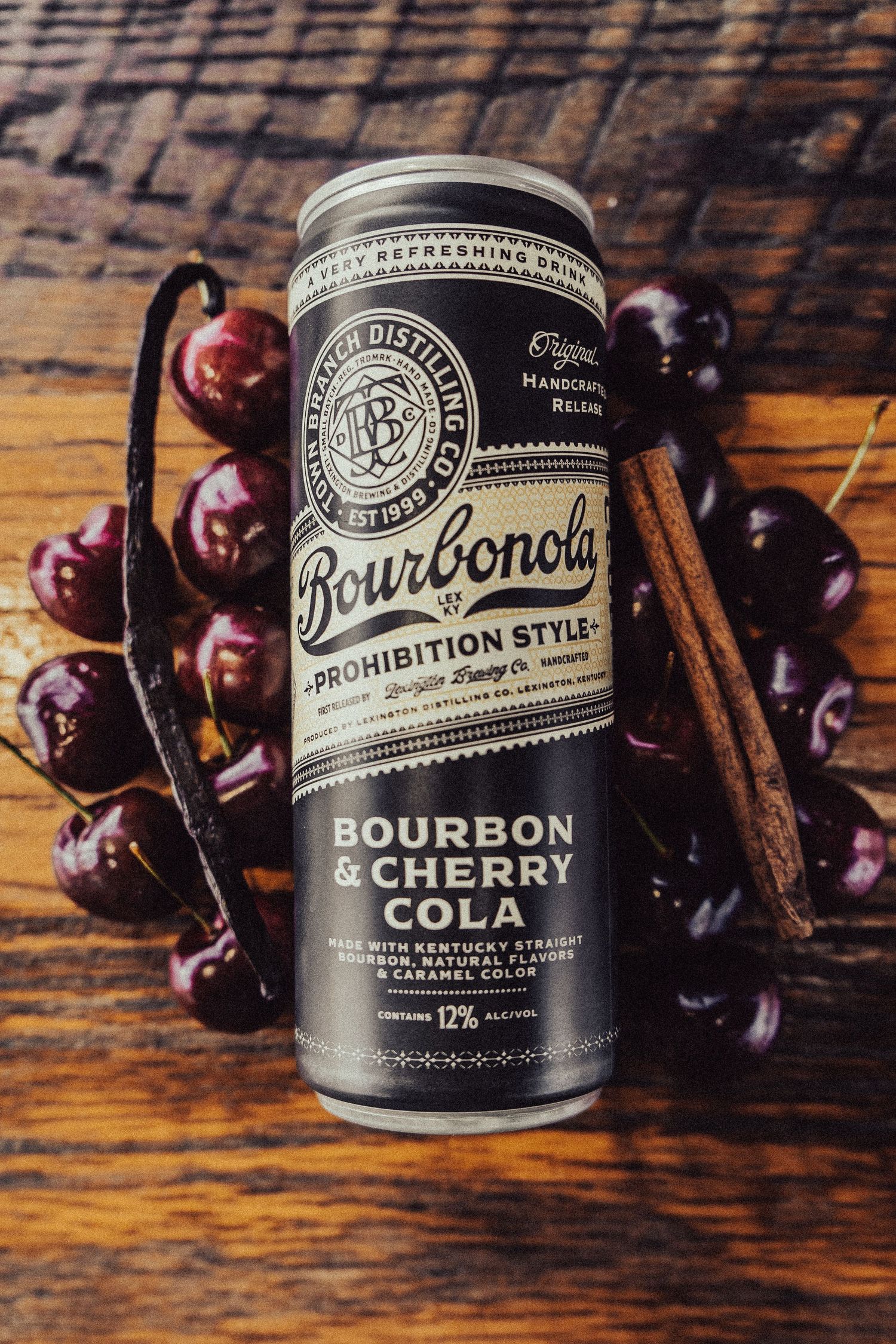 Bourbon cherry cocktail cans displayed with fresh cherries on wooden surface.