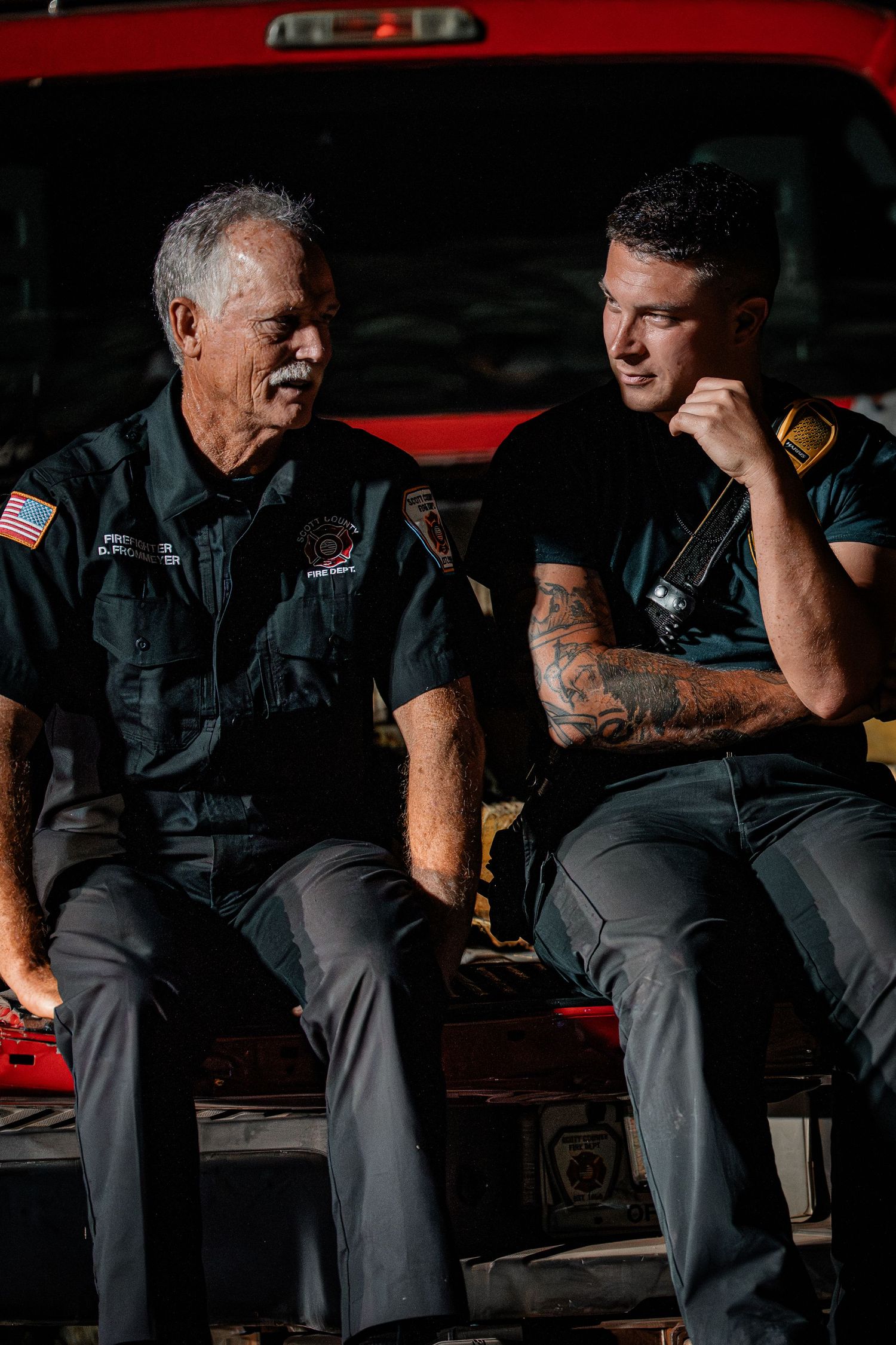 Two firefighters in uniform having a conversation while sitting on their fire truck.