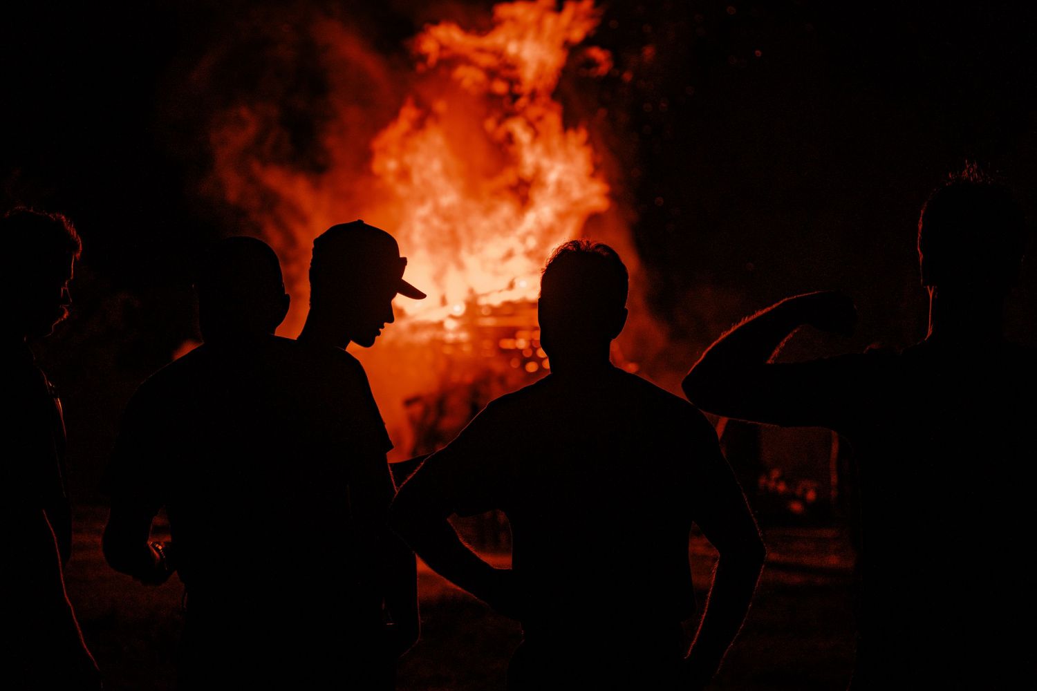 Silhouettes gathered around a large bonfire at night.