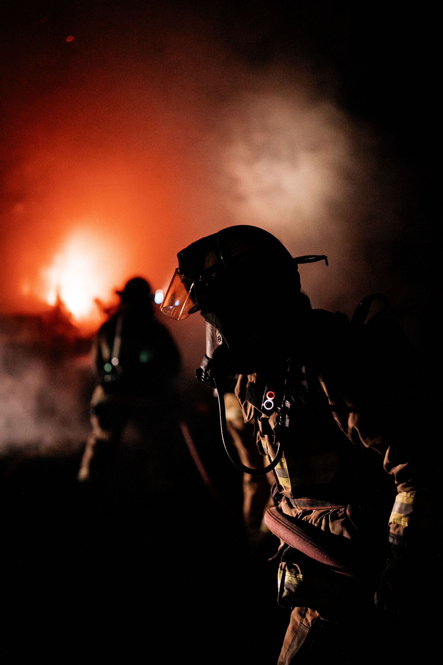 Dramatic silhouettes of firefighters against glowing orange night sky during emergency response.