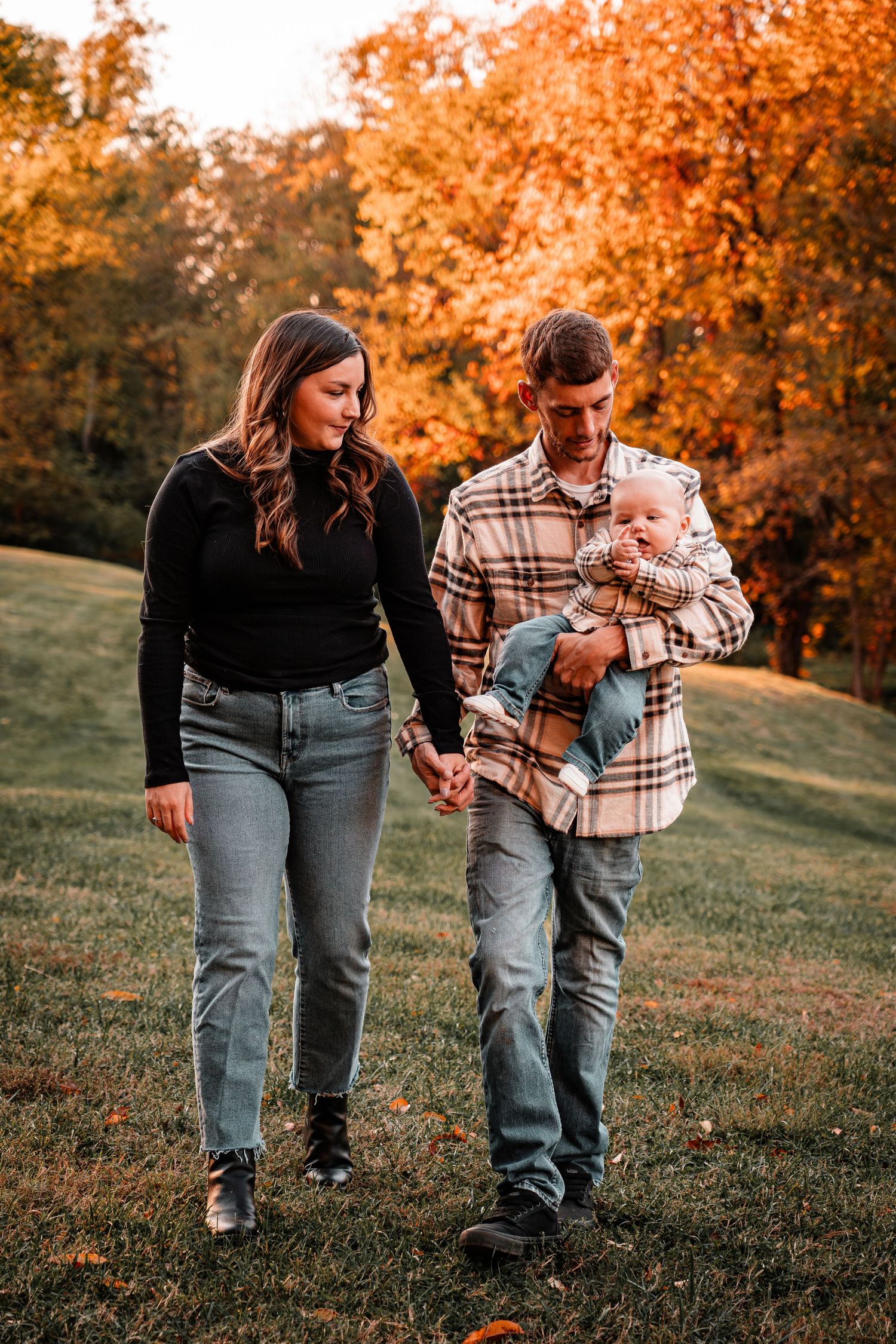 A couple walks hand in hand through an autumn landscape with golden leaves in the background.
