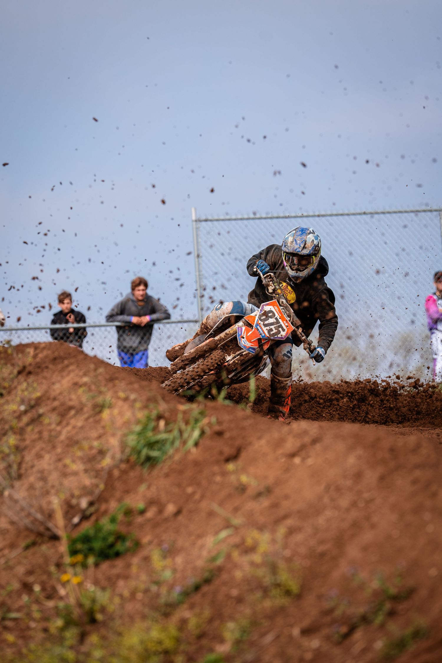 Dirt bike rider sprays soil while cornering steep berm during motocross race.