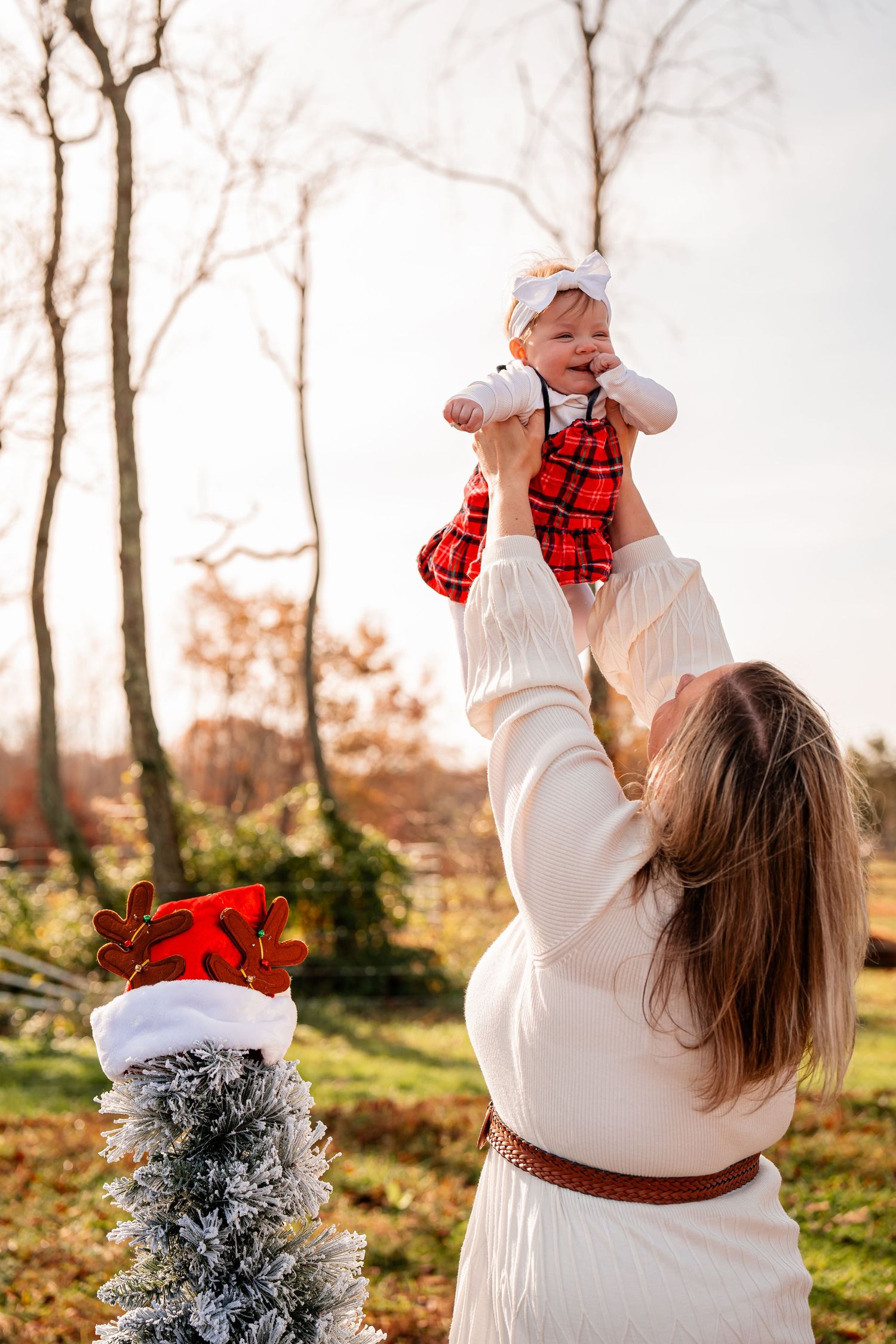 A festive winter scene with someone lifting a baby near a small decorated Christmas tree outdoors.