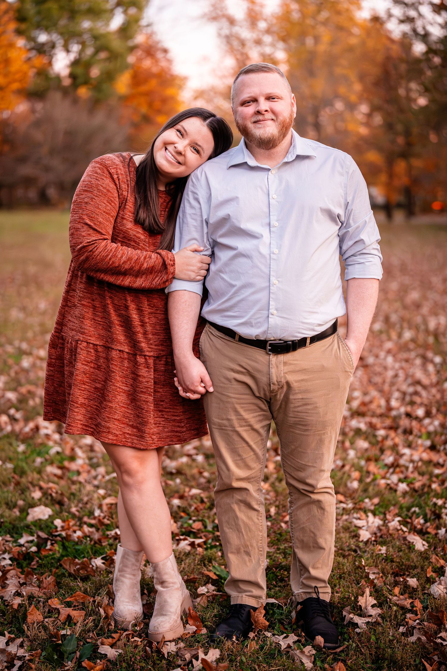 A couple poses together among fallen autumn leaves during sunset.