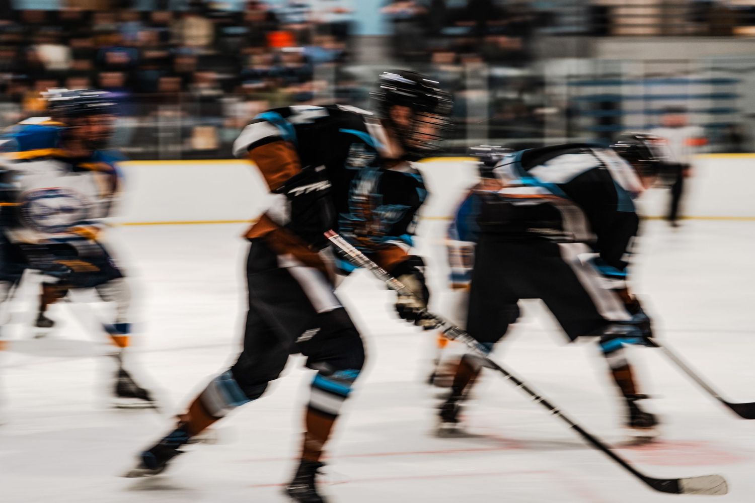 A blurred image of hockey players on the ice, with players in motion and sticks visible.