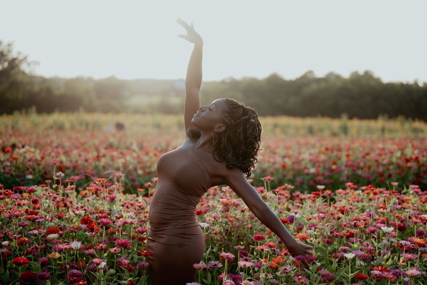 Silhouetted figure stretching gracefully in a field of red flowers at sunset.