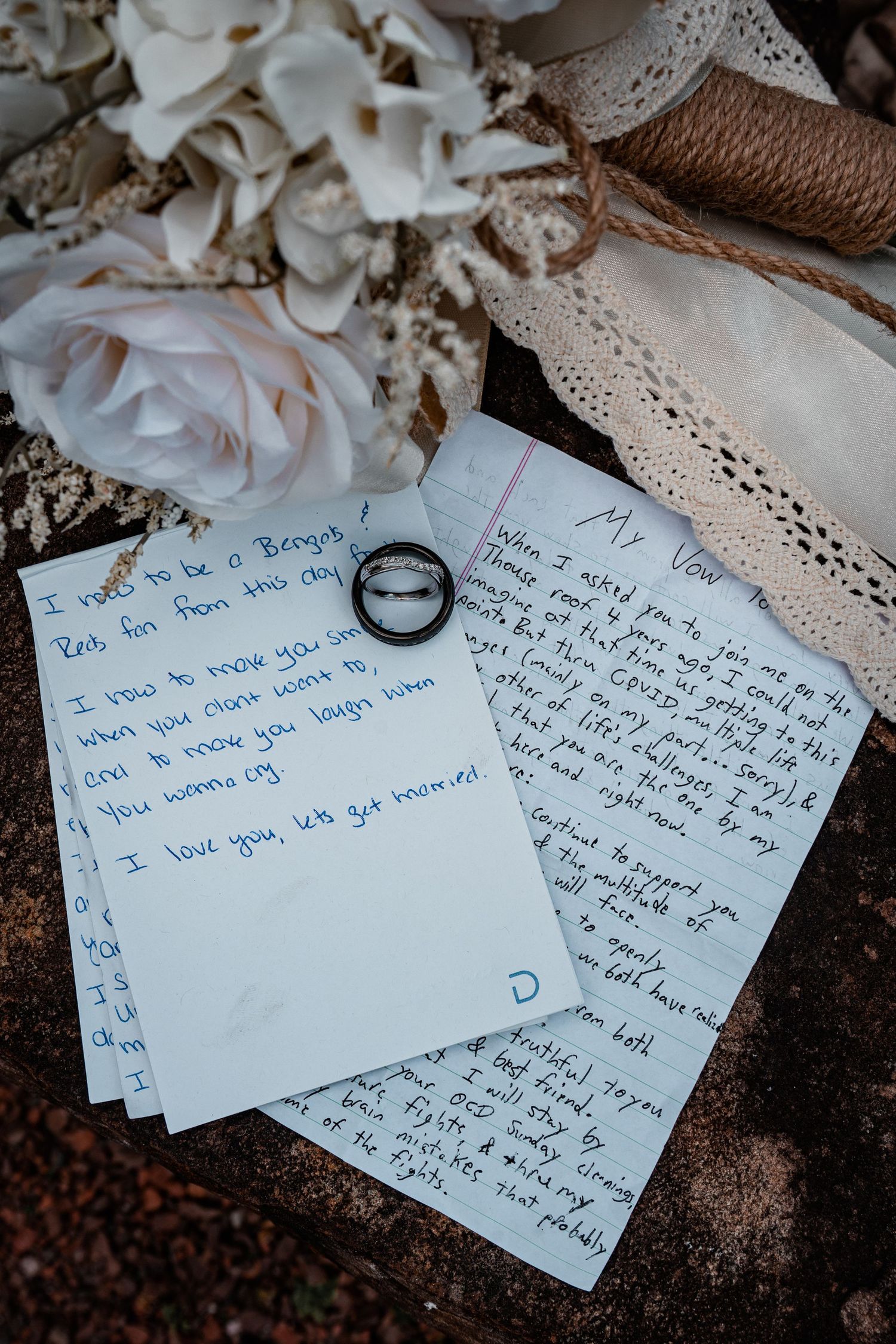 Wedding rings rest on handwritten vows with delicate lace and rose petals.