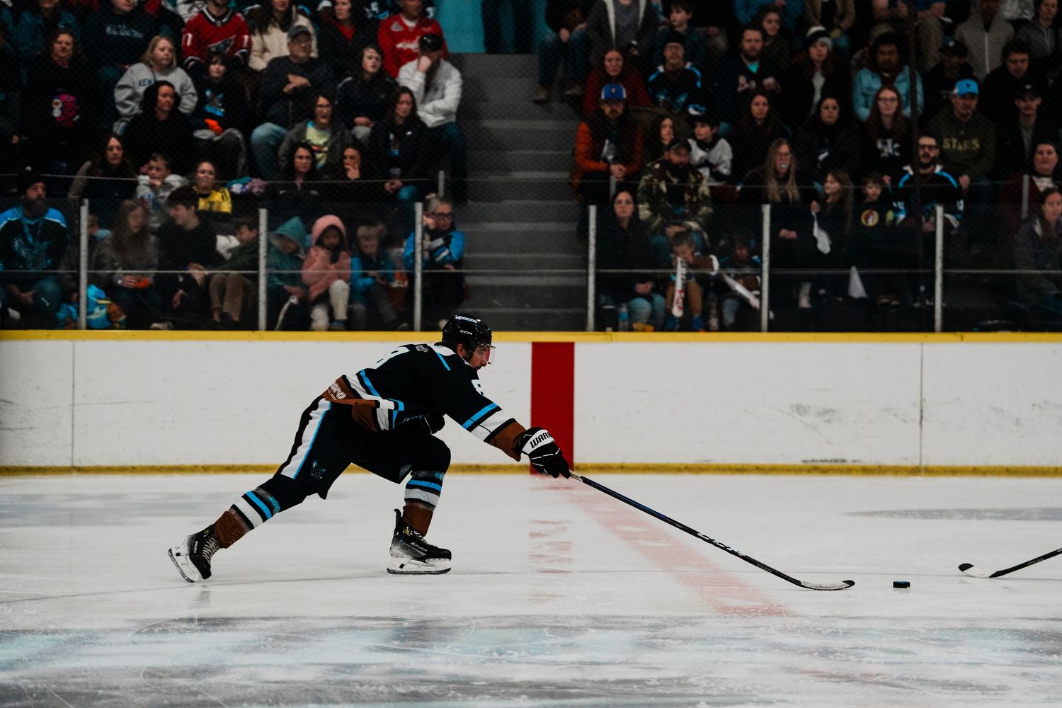 A hockey player in a black uniform is shown skating on an ice rink with a hockey stick in hand.
