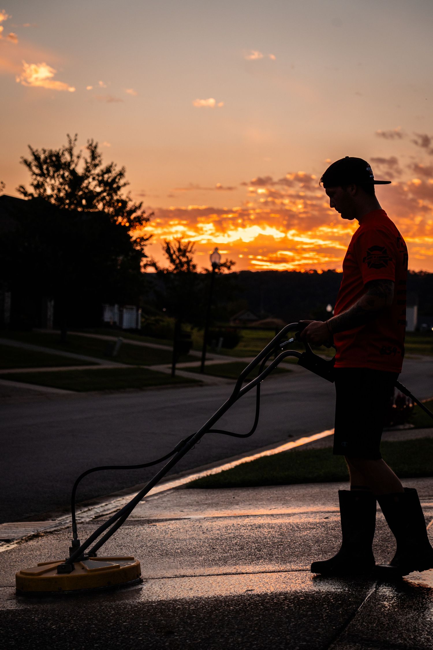 Silhouette of person seal coating asphalt driveway at sunset.