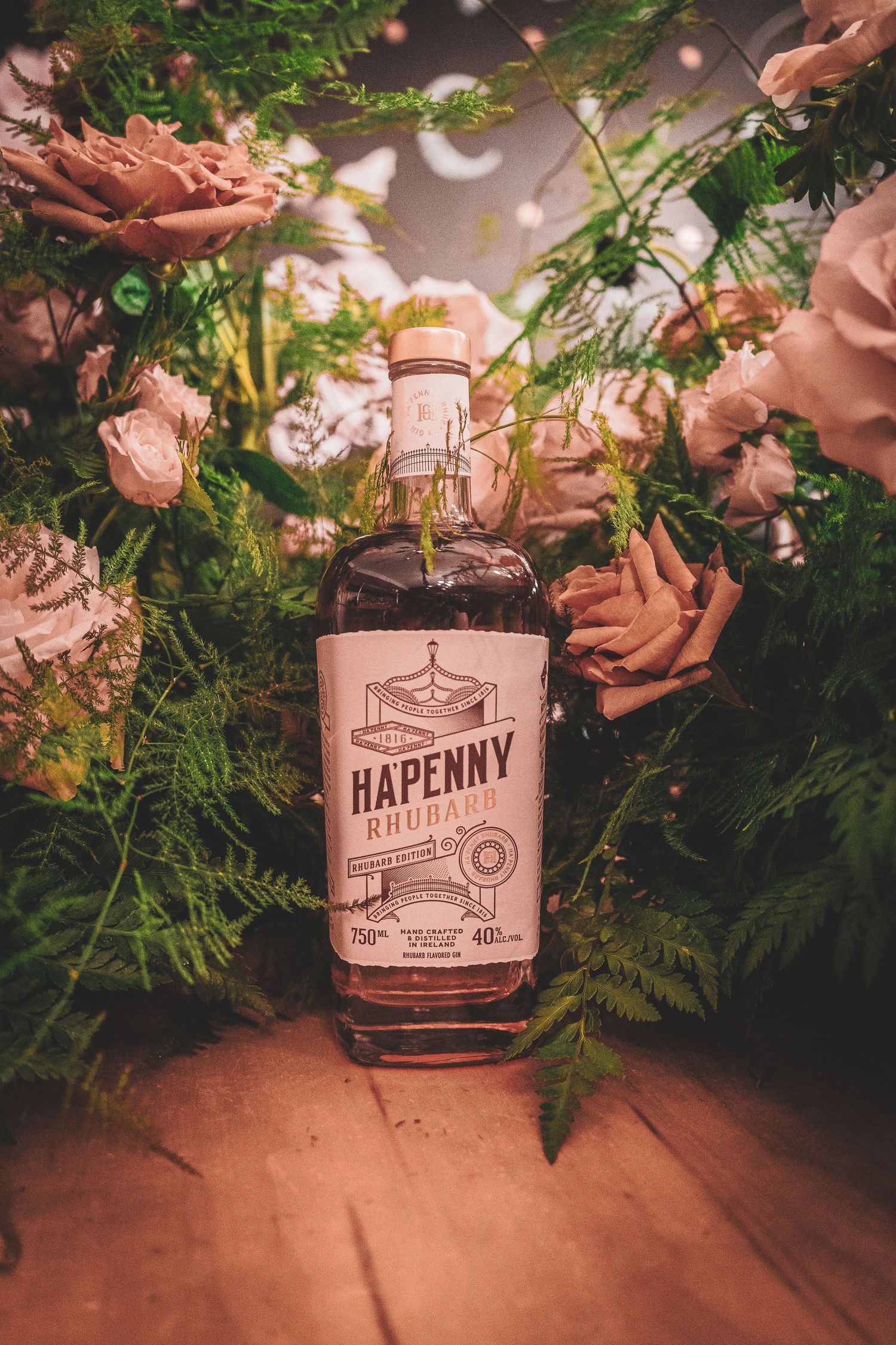 Hapenny bourbon bottle nestled among green ferns and floral decorations.