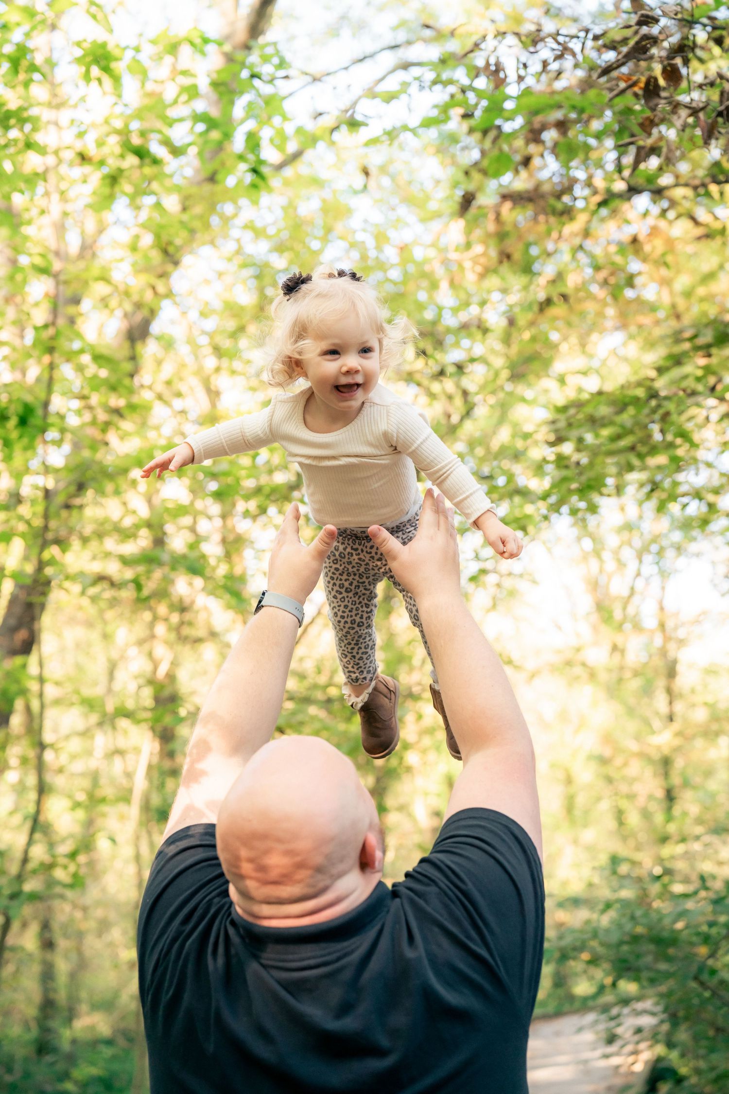 Sequence showing child being lifted into sunlit air among trees in a park setting.