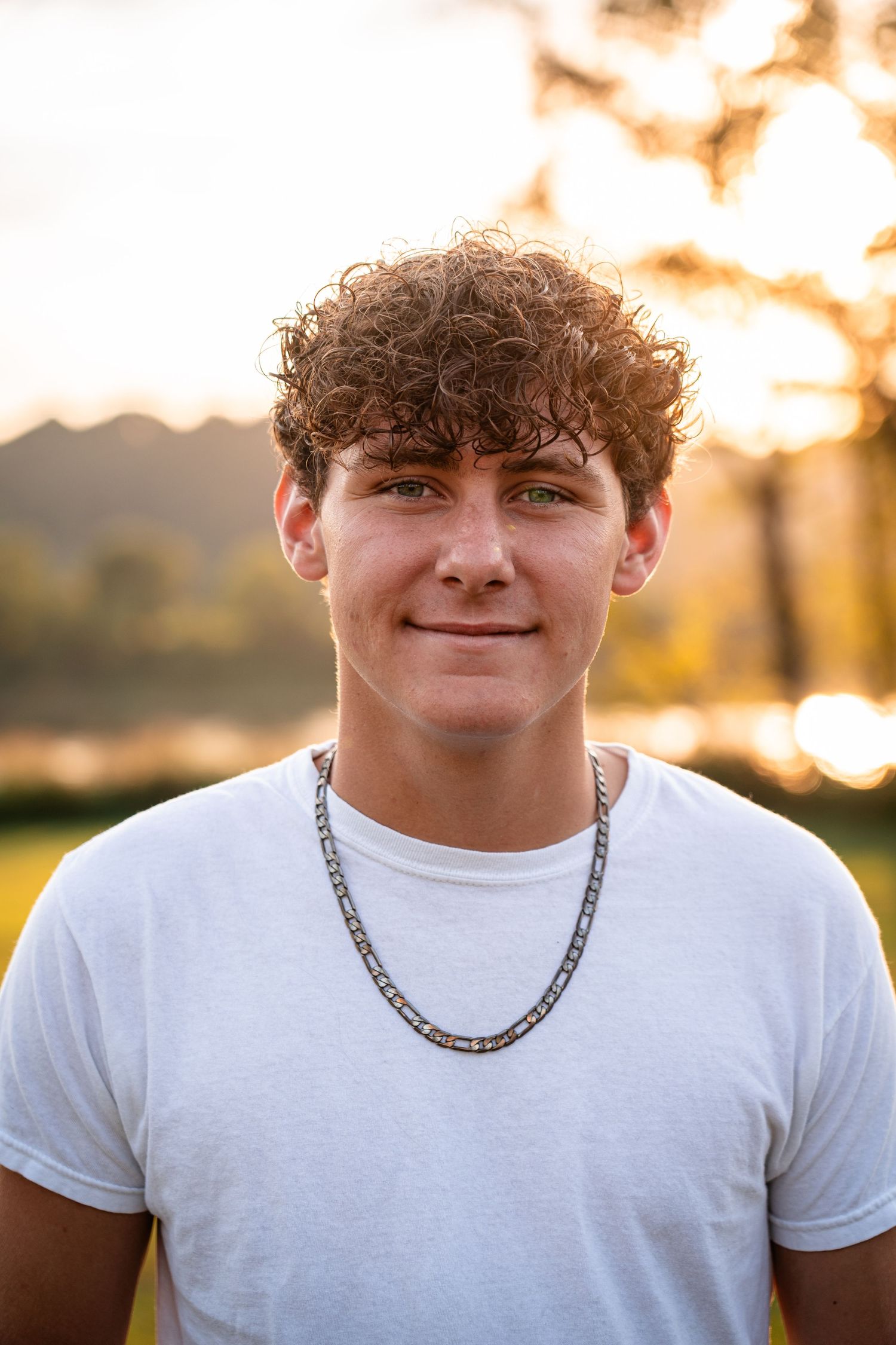 Portrait of young person in white t-shirt and chain necklace at sunset.