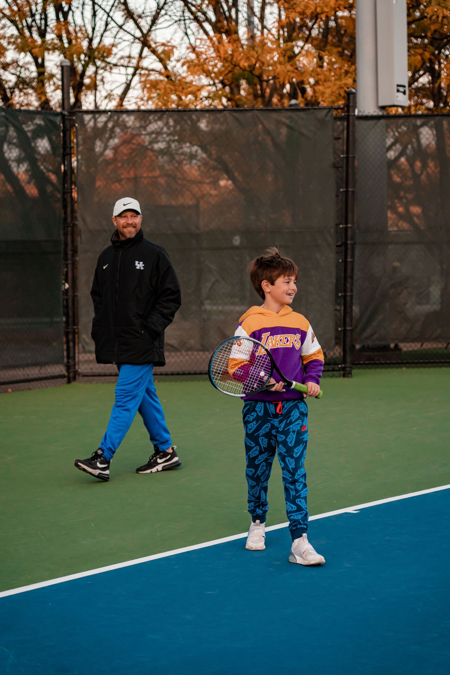 Tennis practice session on outdoor court at sunset with player and coach.