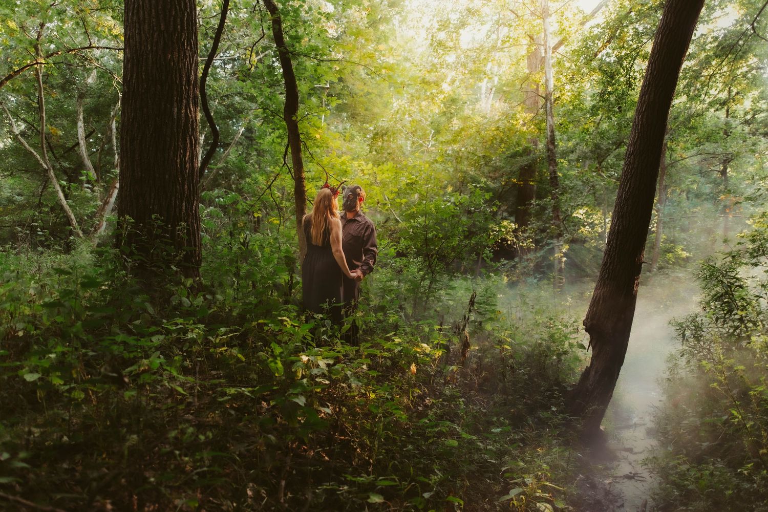a couple dressed up as Persephone and hades for a fantasy session in the middle of the woods with fog rolling through and sun light streams