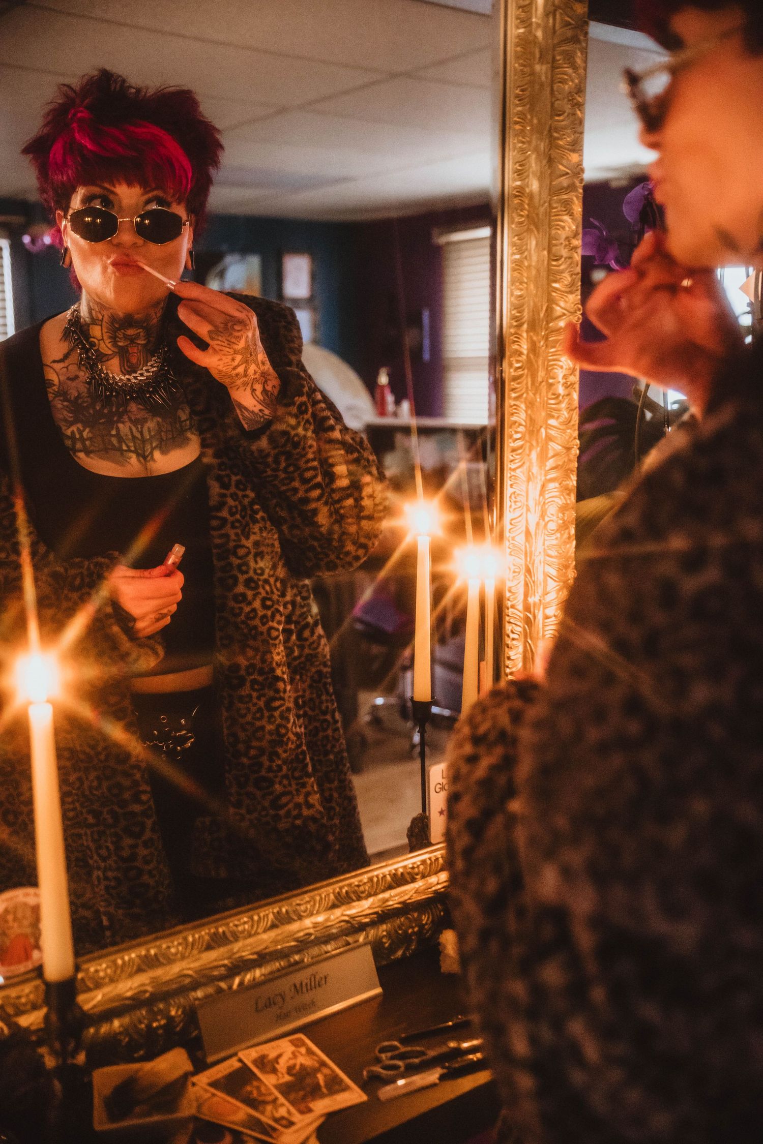 woman putting on lip gloss in mirror with candles lit