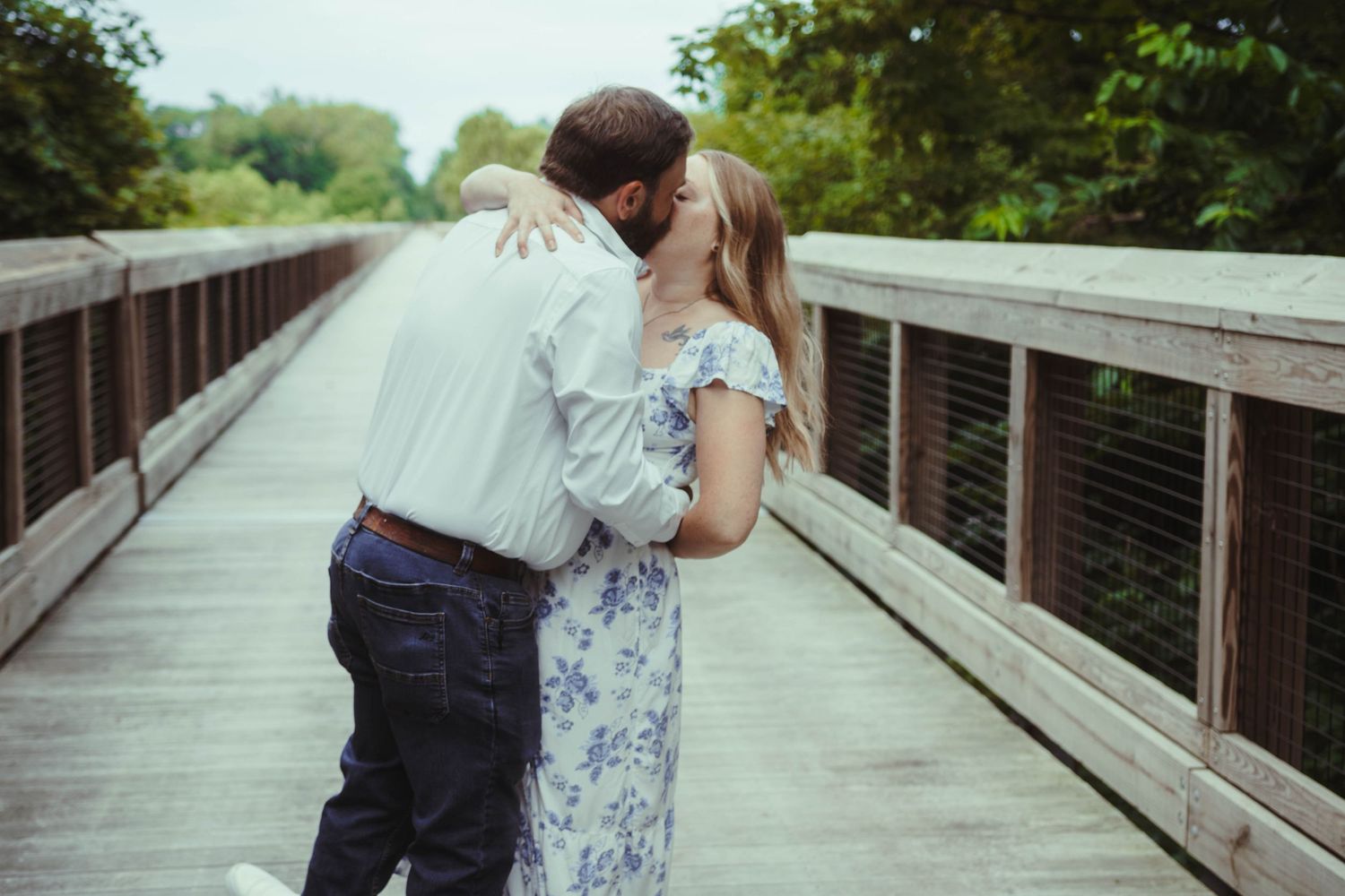 Couple dancing & kissing on the Kickapoo rail trail bridge with green trees all around.