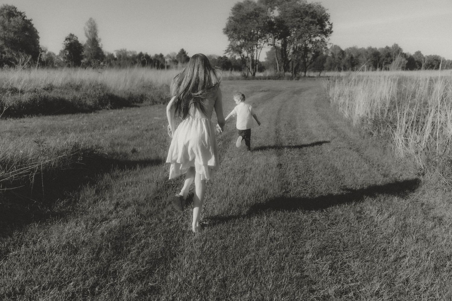 two children running in a prairie. black and white cinematic photograph