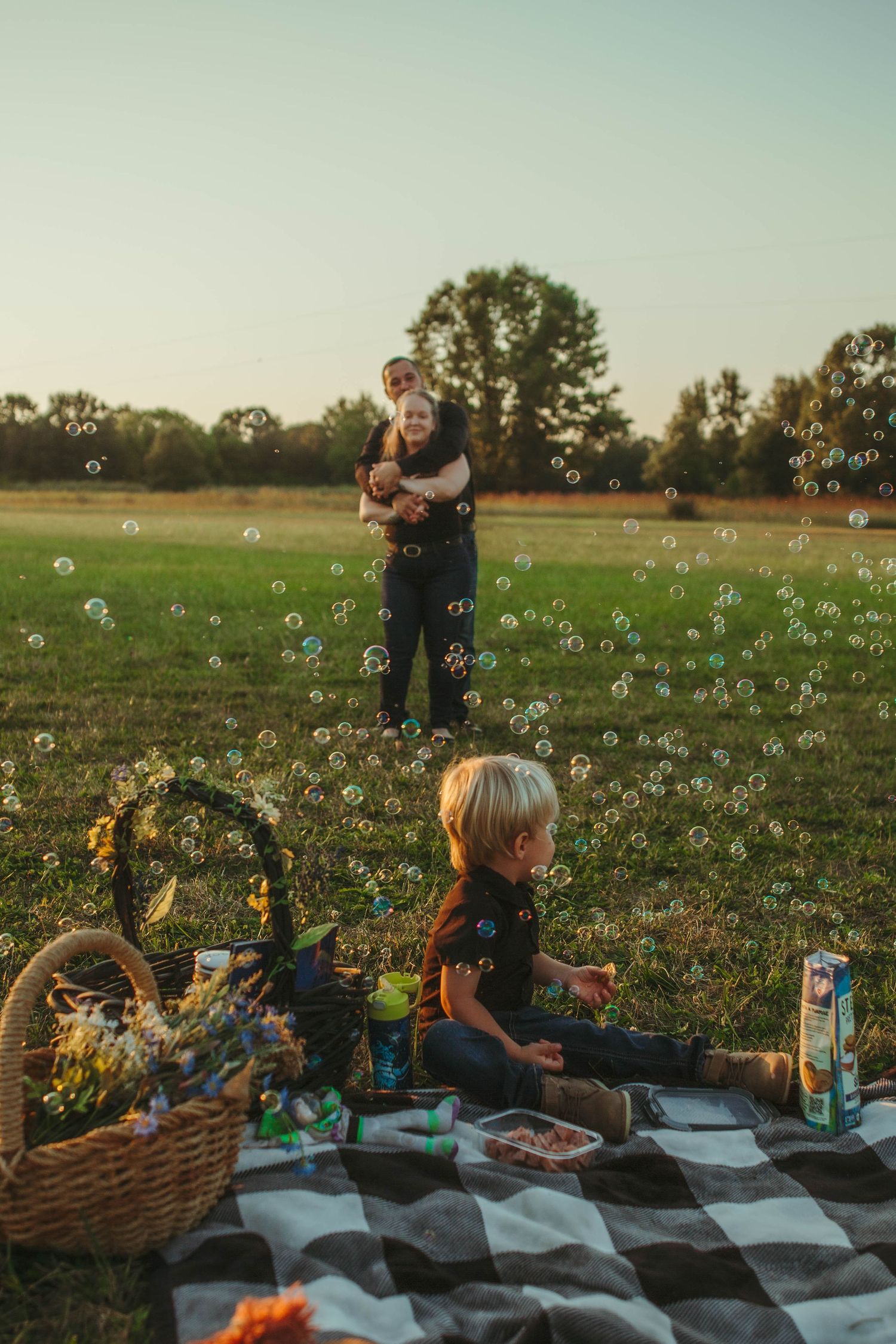 couple hugging with young son sitting on a picnic blanket with bubbles flowing everywhere