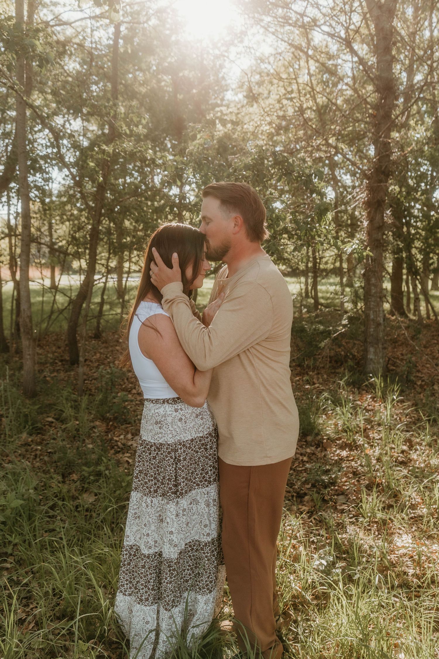 husband and wife embracing in golden glow of sun shining through the woods
