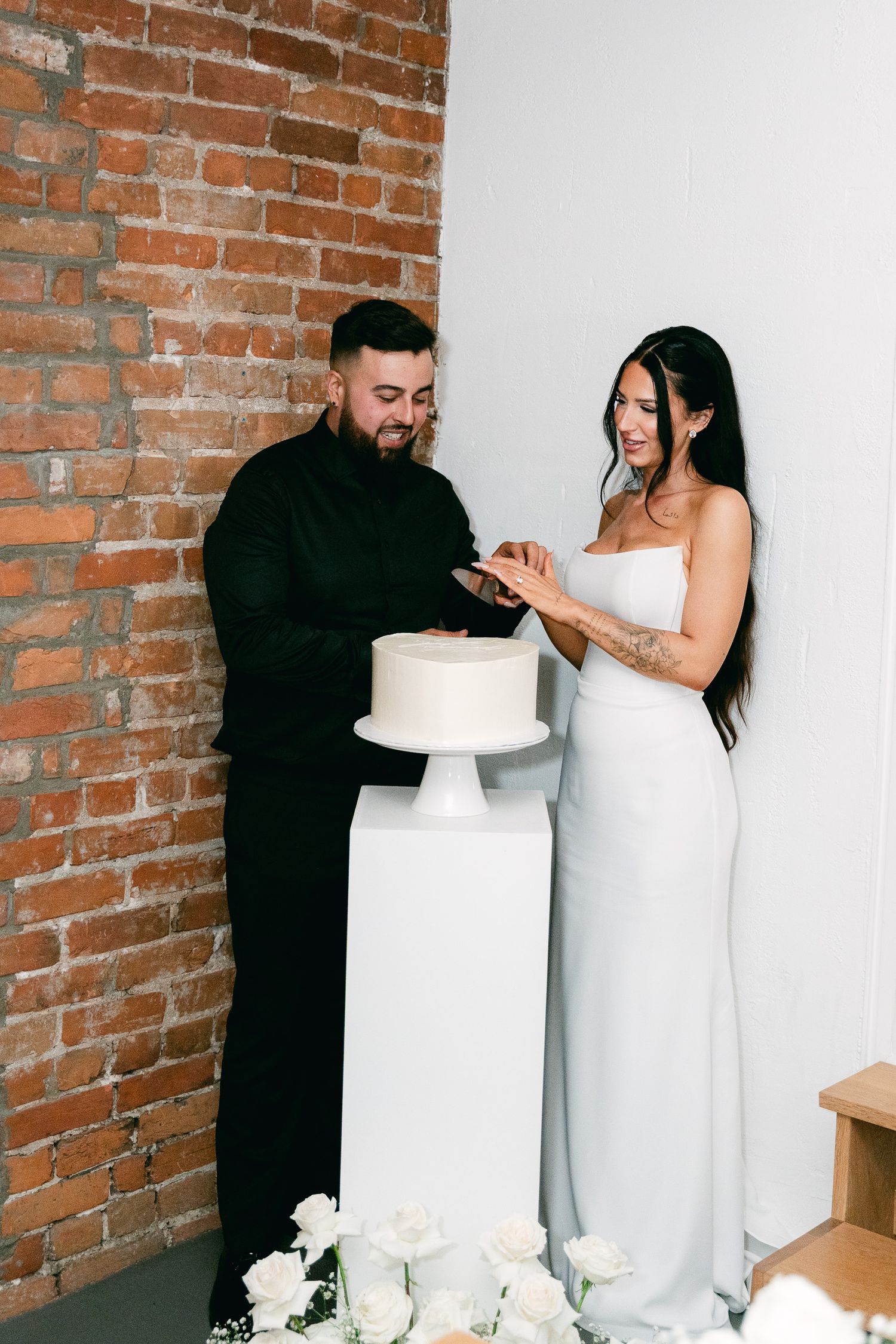 Bride in white dress and groom in black suit cut their wedding cake together.
