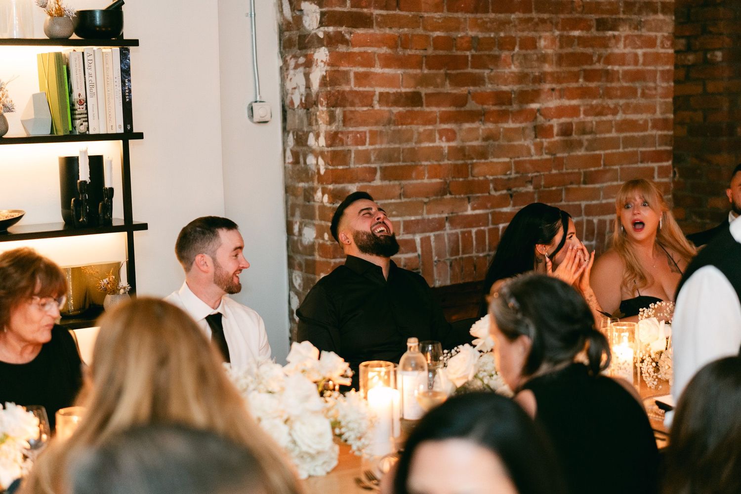 Guests enjoying dinner and conversation at a rustic wedding reception with brick walls and candlelight.