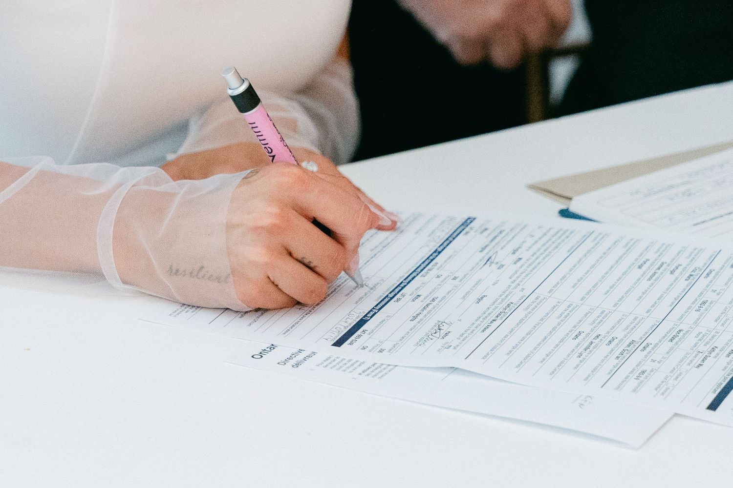 Close-up of hands signing wedding documents on a white table.
