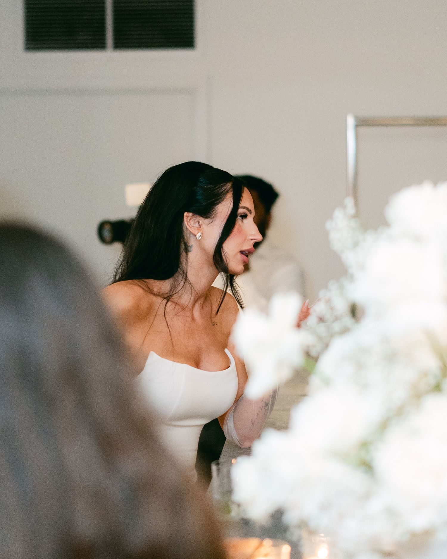 A bride in a white strapless dress surrounded by ethereal floral decorations.