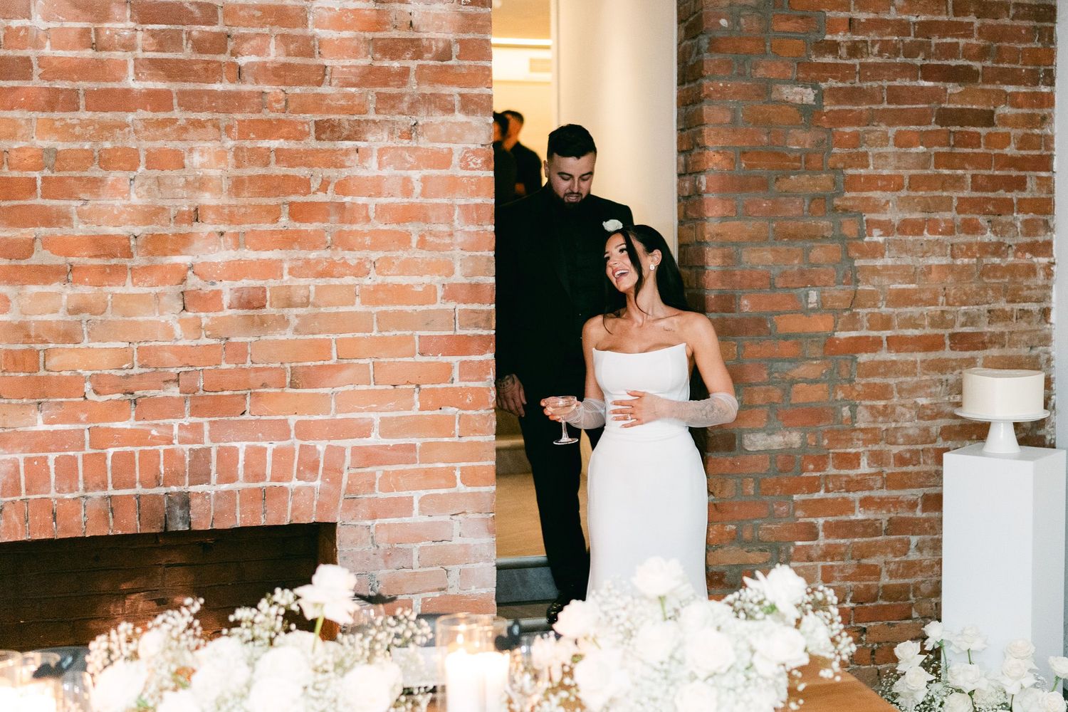 An elegant wedding reception venue with exposed brick walls and white floral centerpieces.