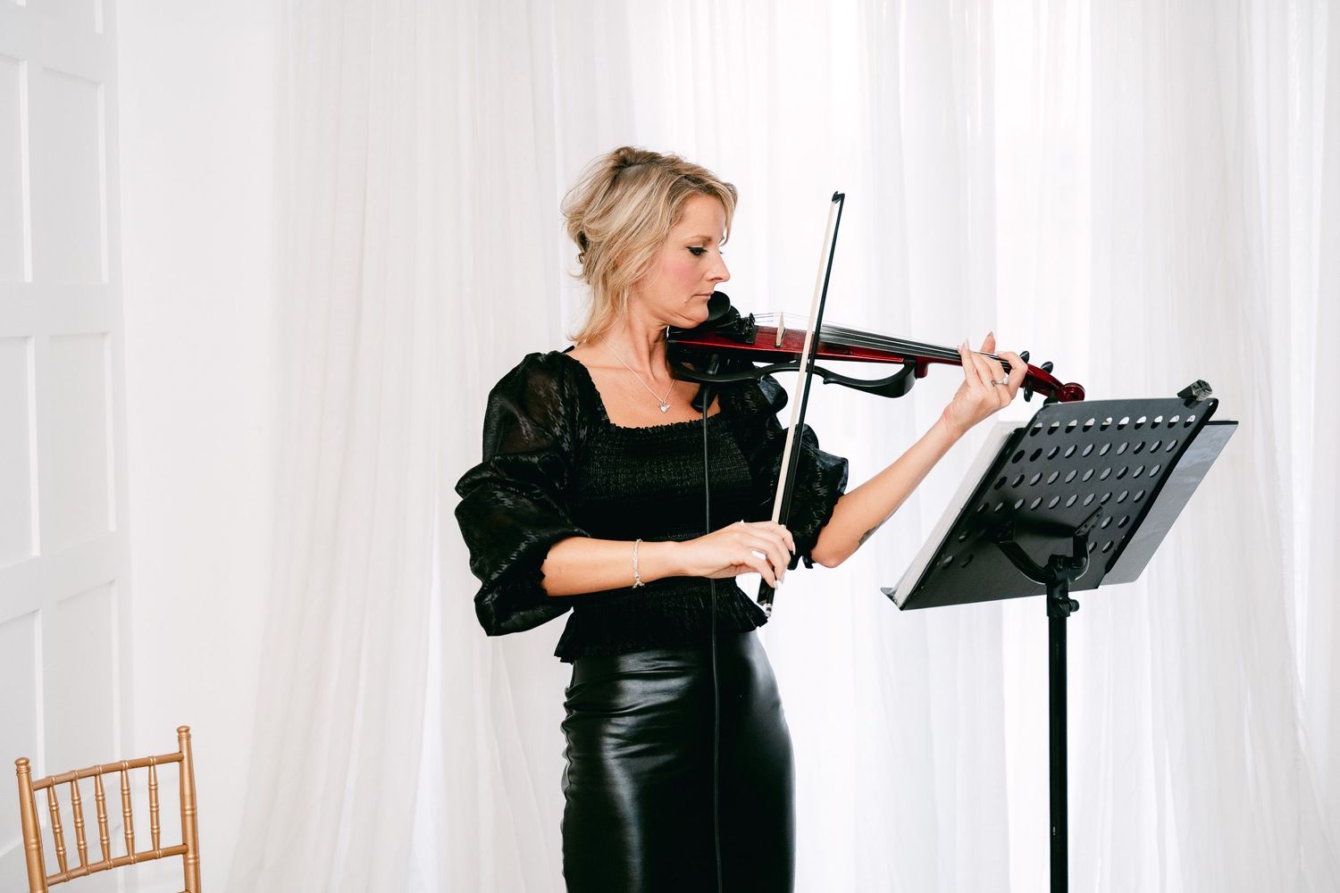 Violinist performing at a wedding ceremony in front of white curtains.