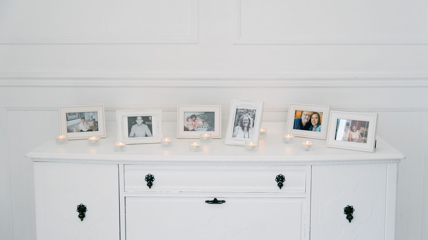 Row of framed photographs displayed on white wall with black hooks.