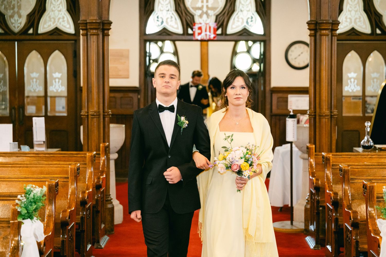 Bride in yellow gown and groom in black tuxedo walking down church aisle during wedding ceremony.