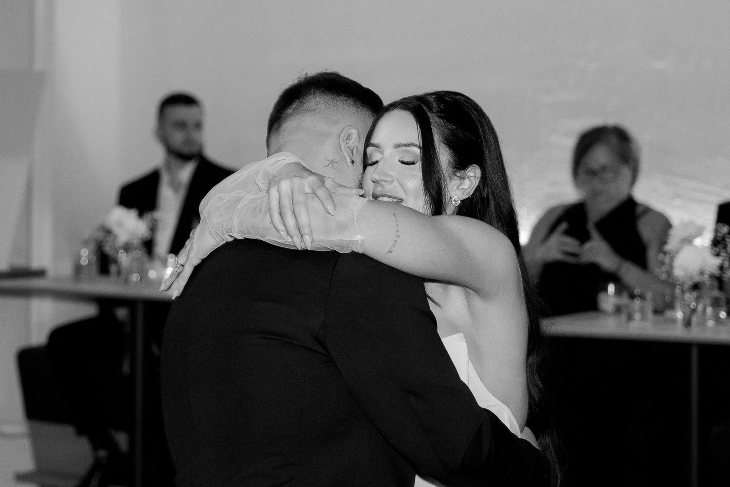 Wedding guests dance in elegant formal attire at an indoor reception venue.