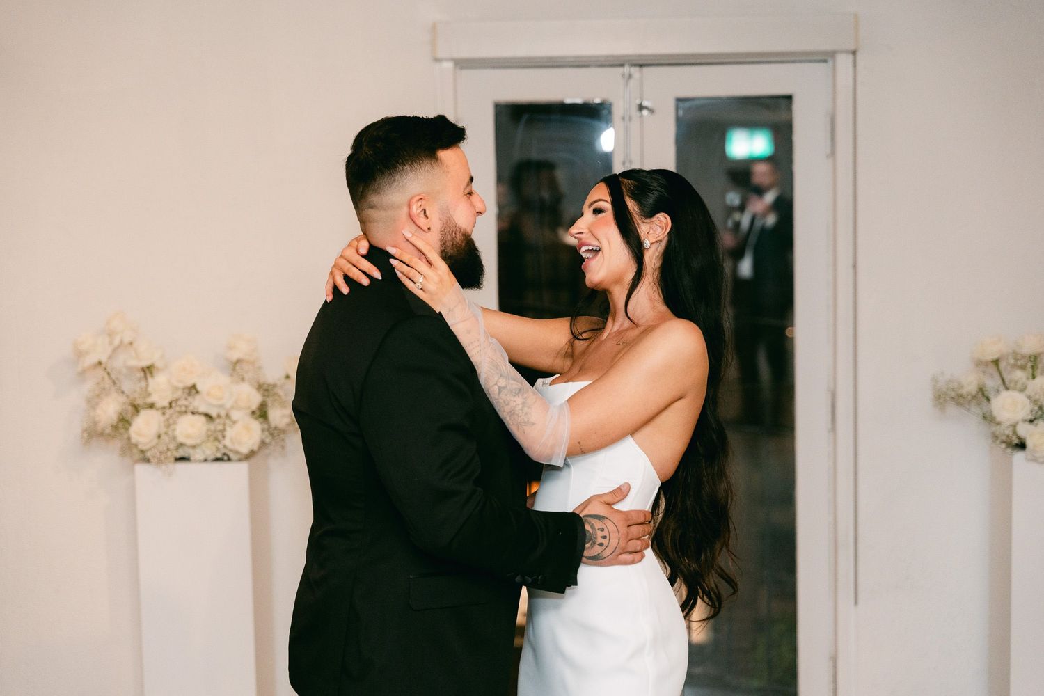 A romantic embrace between newlyweds in front of white floral decorations.