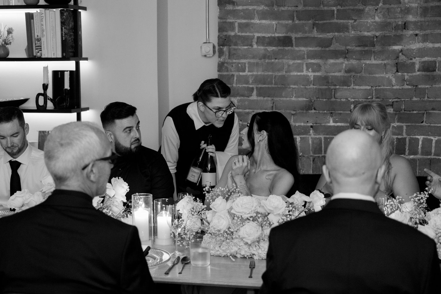 Long table setup at wedding reception with exposed brick walls and elegant floral centerpieces.