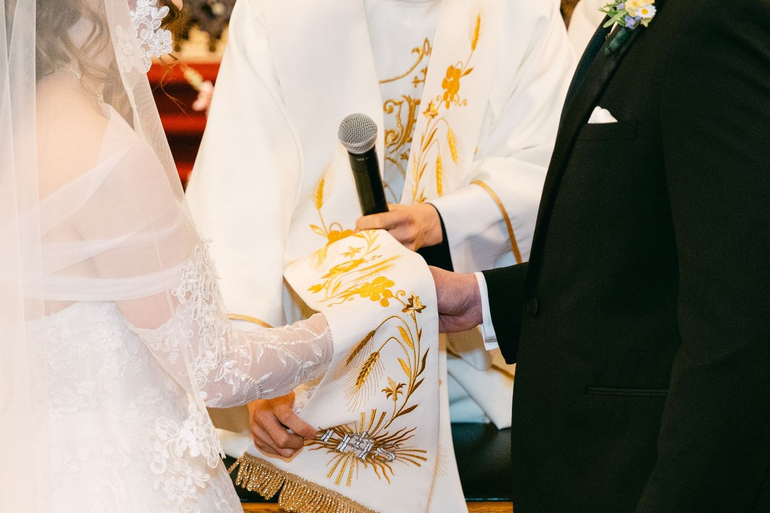 Catholic wedding ceremony with bride and groom exchanging vows before a priest holding a microphone.