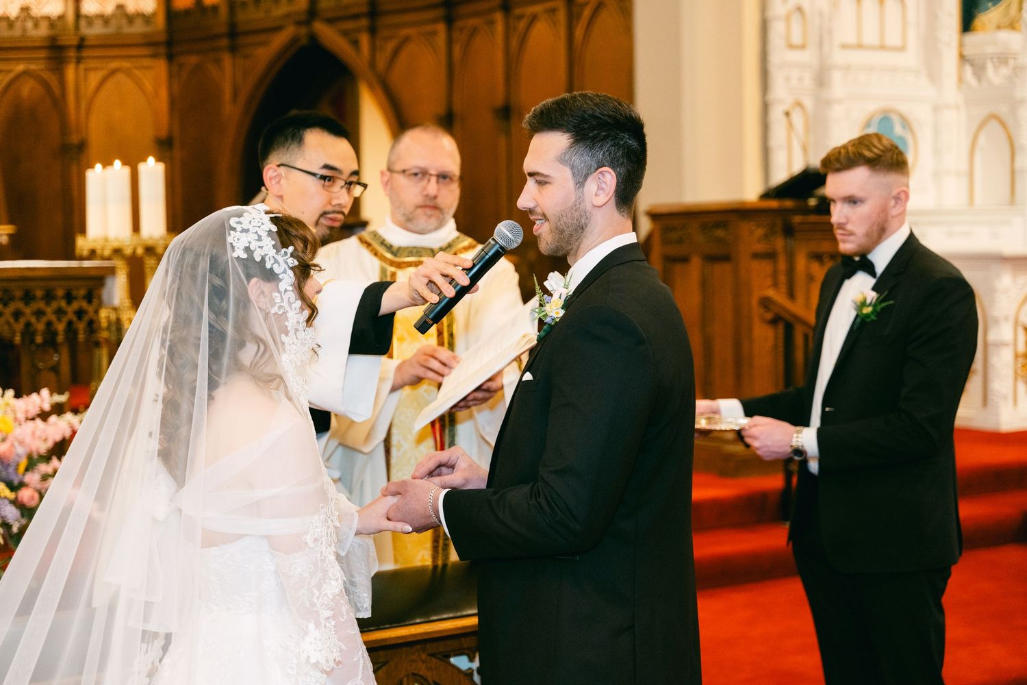 Groom reads wedding vows to bride at church altar with officiant and groomsman standing nearby.