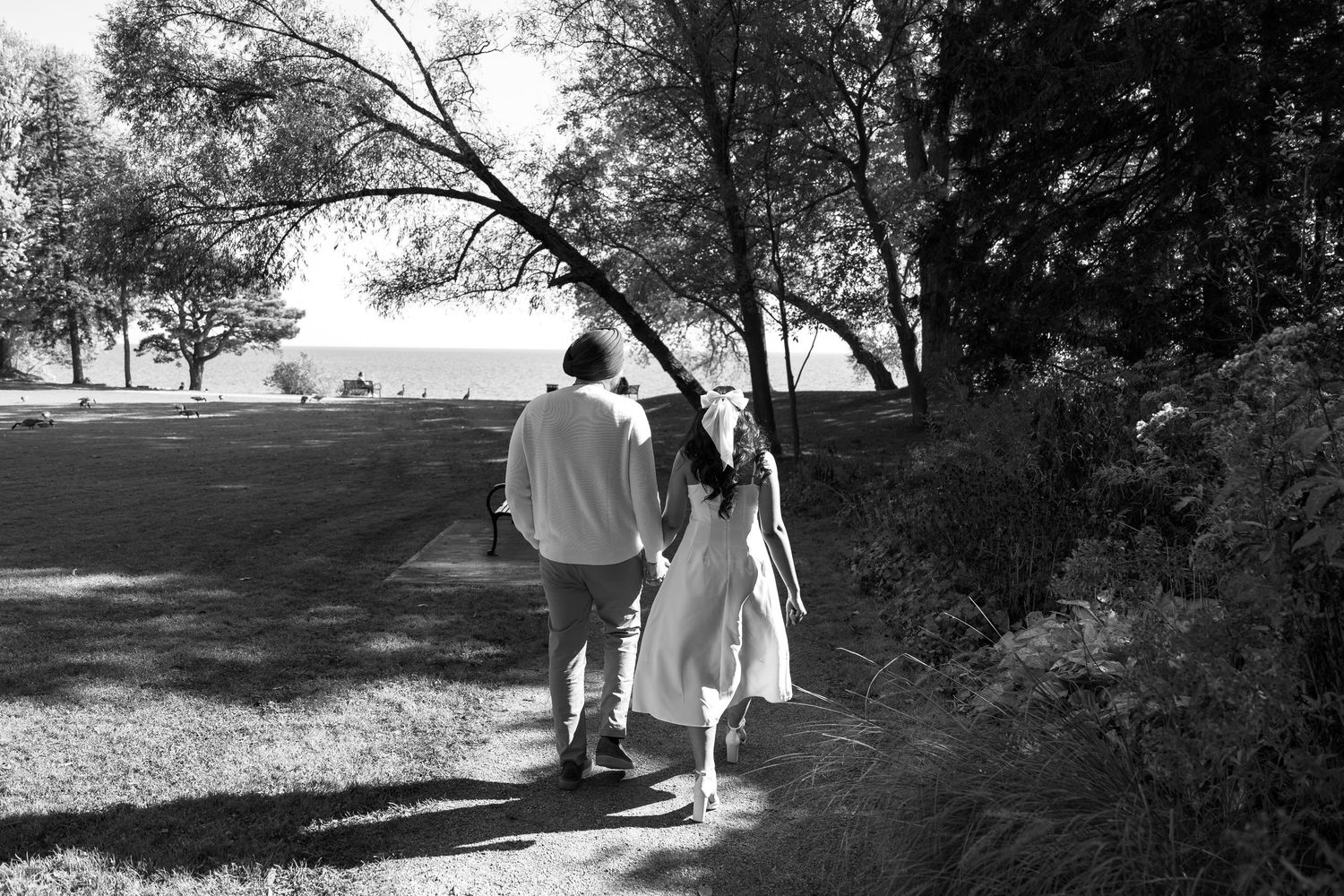 Black and white photograph of couple walking along waterfront nature path.