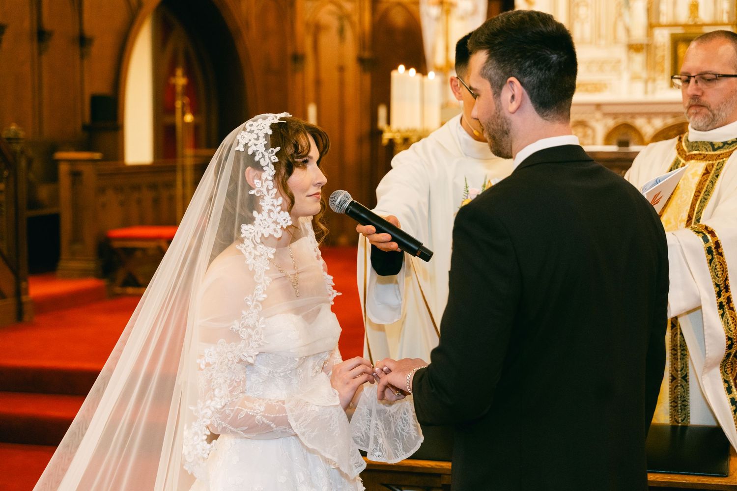 Bride and groom exchanging vows at church altar, bride in lace wedding dress and veil holding microphone.