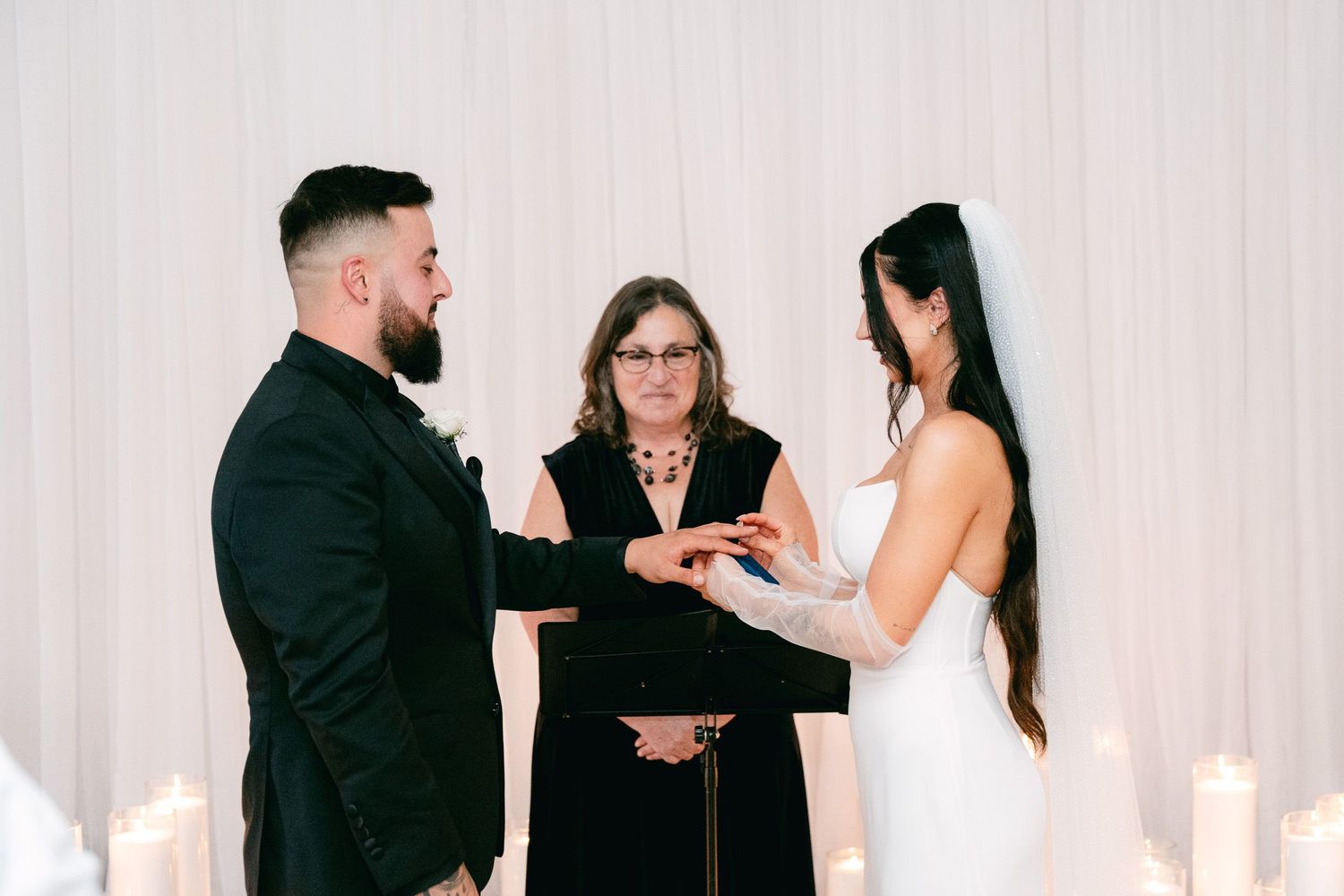 Wedding ring exchange ceremony led by officiant surrounded by candles.
