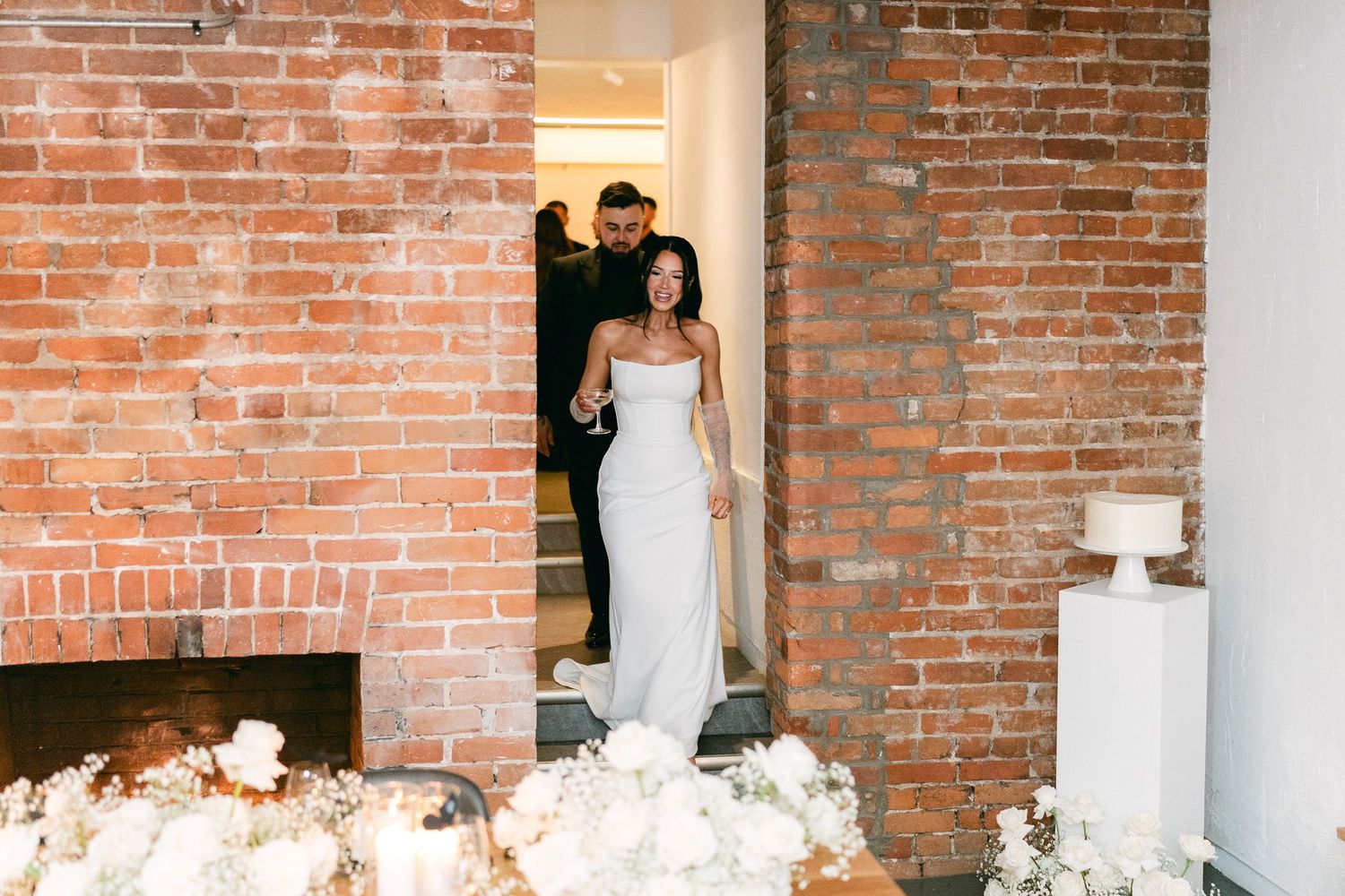 Industrial chic wedding venue with exposed brick walls decorated with white floral arrangements.