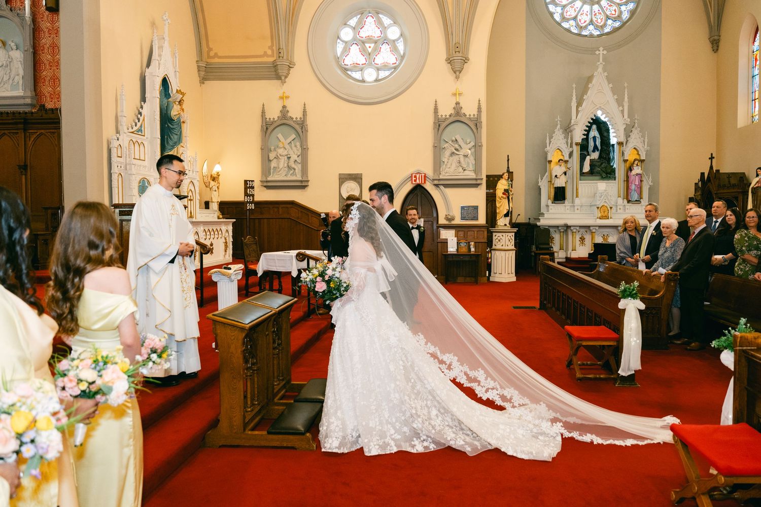 Bride and groom exchanging vows at a traditional church wedding ceremony with a long veil and floral arrangements.