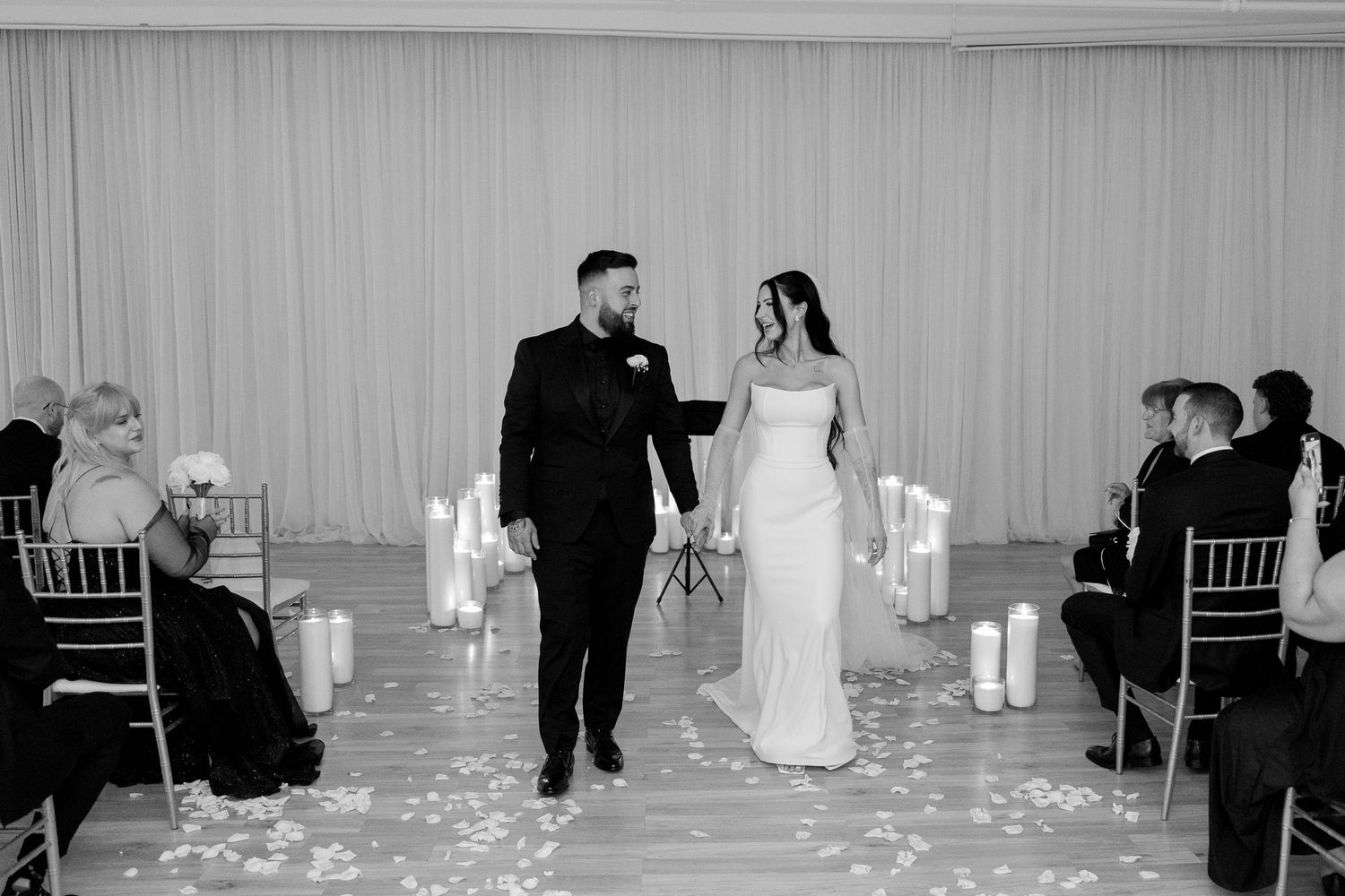 Black and white wedding ceremony photo with chairs and candle decorations.