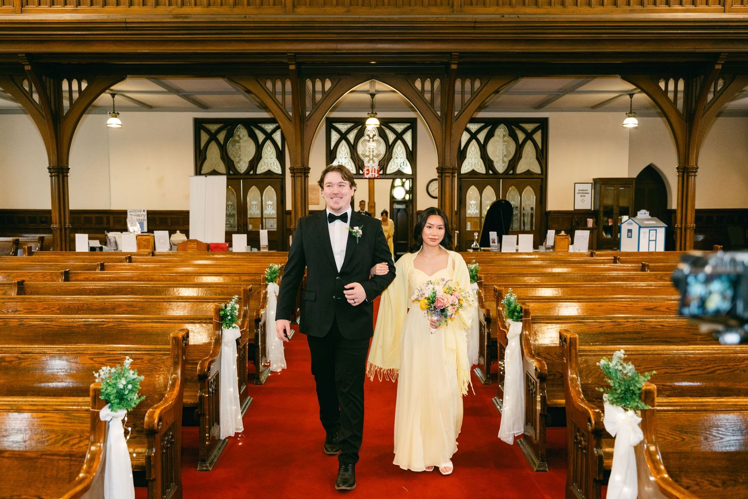 Bride and groom walking down red carpet aisle in elegant wooden church after wedding ceremony.