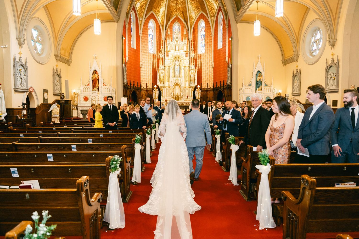 Bride walks down the aisle of a decorated Catholic church during a traditional wedding ceremony.