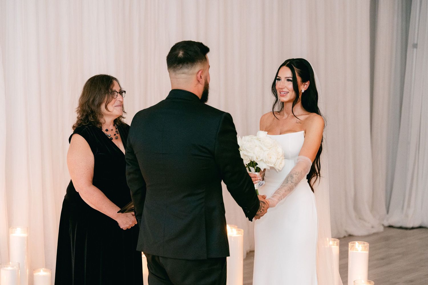Candid wedding moments captured between guests in formal black attire against white drapery.