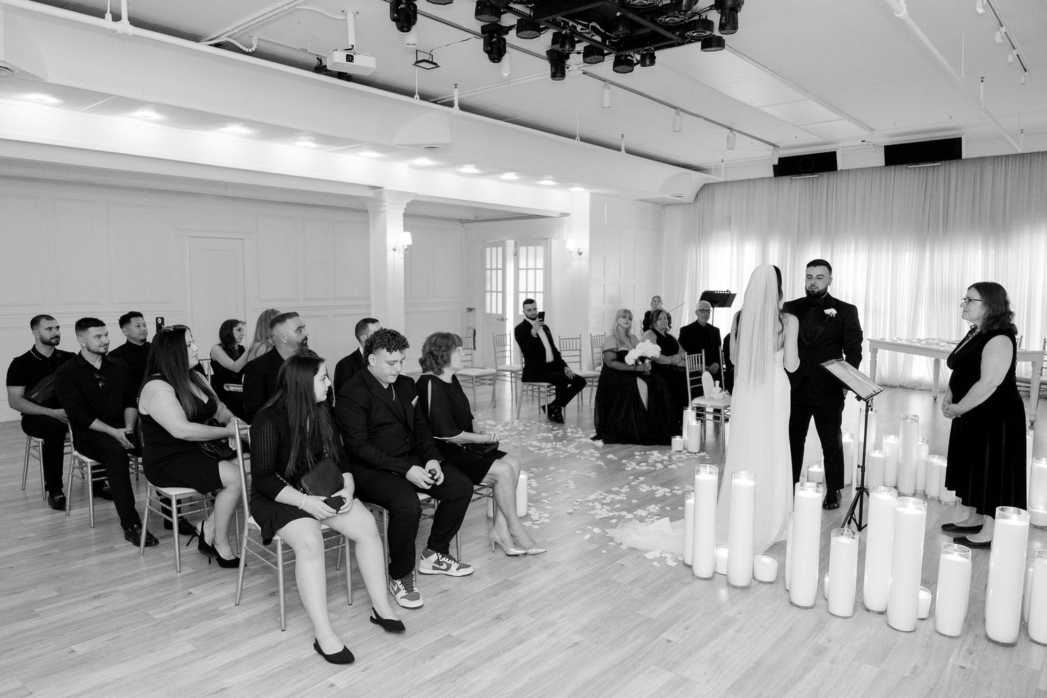 Black and white photo of intimate wedding ceremony with guests seated among white pillar candles.