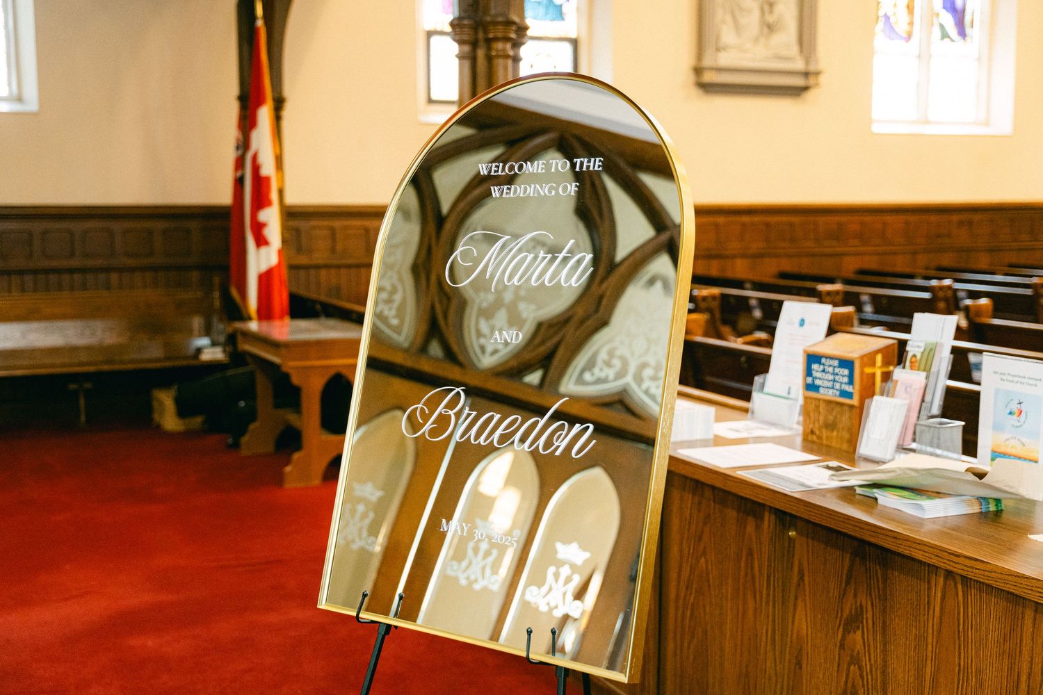 Elegant mirrored wedding welcome sign for Maria and Braeden displayed on easel in a church.